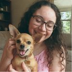 Smilende kvinde med briller holder lille tan chihuahua hund tæt i stue
